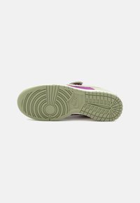 Sneaker with a textured green rubber outsole, featuring circular and linear tread patterns. Includes a pink accent on the side.