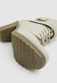 Botín beige hasta el tobillo con parte superior de ante texturizado, diseño de cordones y tacón de bloque. La suela de goma cuenta con un dibujo en relieve para una mejor tracción.