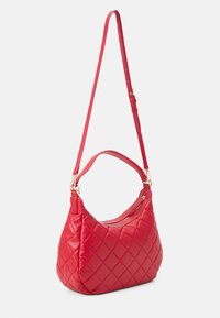 Sac à main matelassé rouge avec une forme incurvée, doté d'une longue bandoulière réglable et de garnitures en métal doré. Texture lisse et fermeture éclair détaillée.