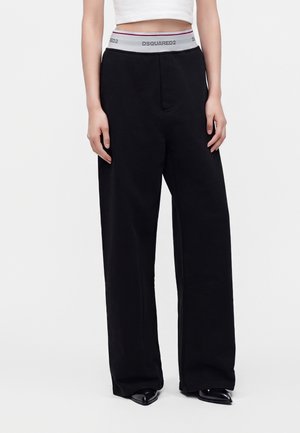 Personne portant un pantalon noir à jambes larges avec une ceinture élastique grise portant l'inscription DSQUARED2 et un top court blanc.