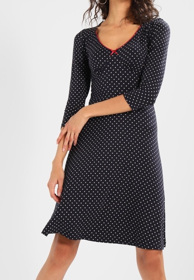 Navyblaues Kleid mit weißen Polka-Dots, Dreiviertelärmel, V-Ausschnitt und rotem Paspelierungsdetail an Kragen und Taille. Ausgestellter Saum.