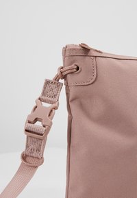 Borsa in tessuto rosa con finitura testurizzata, dotata di chiusura a zip e clip in plastica sulla tracolla per lunghezza regolabile.