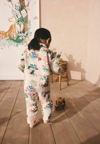 Puuvillane pidžaama komplekt, millel on hele kreemitaust ja värvikad looma- ja lillemustrid. Esiplaanil on puust mänguauto, kõrval tool.