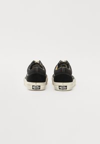 Baskets en daim noir avec semelles en caoutchouc blanc, coutures contrastées et détail du logo à l'arrière. Bout arrondi et design bas.