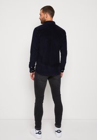 Mörkblå kordflugekjorta med långa ärmar, knappmanschetter och svängd nederkant, kombinerad med slim-fit mörka jeans och vita sneakers.