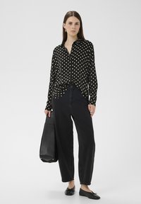 Fekete pöttyös, gombos hosszú ujjú ing, magasan szabott fekete farmernadrággal párosítva. Kiegészítőként fekete táska és lapos talpú cipő viselve.