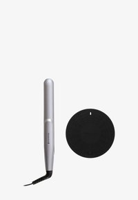 Piastra per capelli argentata e slanciata con punta arrotondata, accompagnata da un tappetino circolare nero resistente al calore con un motivo geometrico.