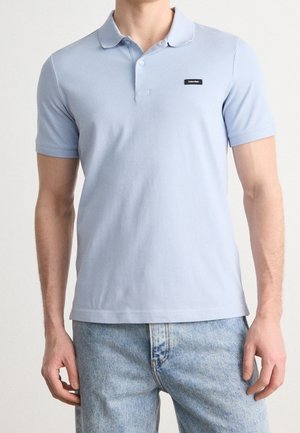 Jasnoniebieska koszulka polo z miękkiej bawełny, z klasycznym kołnierzykiem, krótkimi rękawami i małą naszywką z logo po lewej stronie klatki piersiowej.