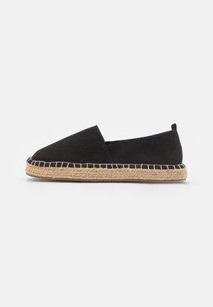 Espadrille en toile noire avec semelle en jute tressée naturelle, style slip-on et talon bas, montrée de profil sur fond blanc.