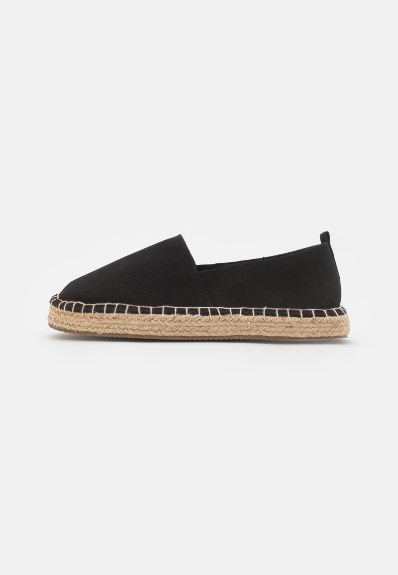 Espadrille en toile noire avec semelle en jute tressée naturelle, style slip-on et talon bas, montrée de profil sur fond blanc.