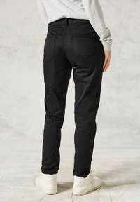 Svarta slim-fit byxor i ett mjukt tyg med bakfickor, bältesömmar och en lätt glans. Matchas med vita högskurna sneakers.