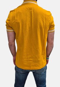 Polo giallo con tessuto testurizzato, dotato di colletto e polsini a righe bianche. La parte posteriore è semplice e ha una vestibilità comoda. Indossato con jeans in denim.