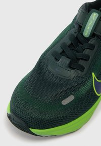 Sapatilha de corrida Nike em verde escuro e preto com sola verde limão, atacadores pretos e rótulo "Stellar Ride" na língua.