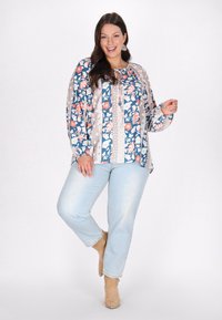 Multi-mønstret bluse med blomsterdesign i blå, pink og beige. Løs pasform med lange ærmer og snøreudskæring. Lyse denim jeans.