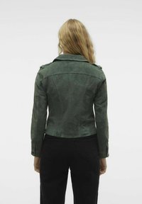 Grüne Wildlederjacke mit tailliertem Design, breitem Kragen und geknöpften Schulterklappen. Der Rücken weist dezente Steppdetails auf.