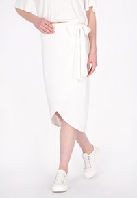 Witte wikkelrok met een strikdetail in de taille, met een zachte textuur en een licht asymmetrische zoom. Gepaarde met witte sneakers.