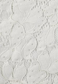 Tessuto bianco con un design in pizzo floreale che presenta foglie testurizzate e piccoli ritagli esagonali, combinato con uno strato di base liscio.