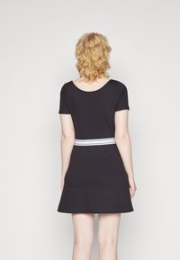 Musta lyhythihainen mekko, jossa on istuva bodice, levenevä hame ja valkoinen vaakasuora raita vyötäröllä. Suloinen kangas, yksinkertainen muotoilu.