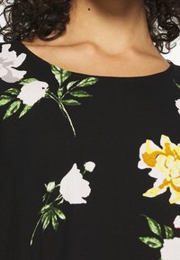 Tissu noir avec un imprimé floral comportant des fleurs blanches, jaunes et vertes. Encolure arrondie et texture lisse, mettant en valeur des couleurs vives.