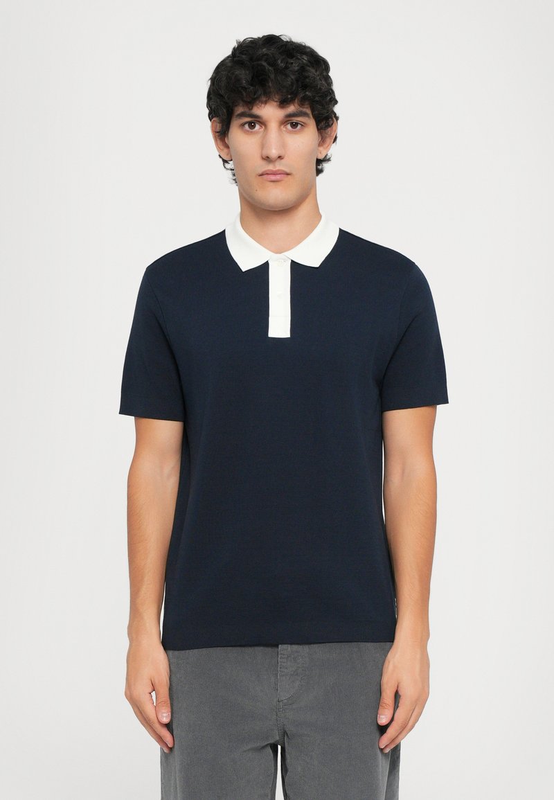 Marineblå polo skjorte med korte ermer, hvit krage og placket. Teksturert stoff, slim fit design, kombinert med grå kordfløyelsbukser.