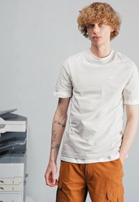 Biela bavlnená tričko s krátkymi rukávmi a okrúhlym výstrihom, s malým logom Nike. V kombinácii s hnedými cargo šortkami.