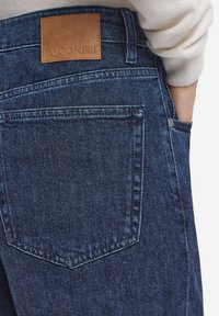 Jeans i mörkblå denim med en texturerad yta, med en lädermärkning som är märkta "FALCONERI" på midjebandet och diskreta fickor.