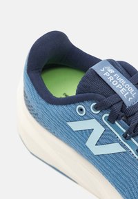 Scarpa sportiva blu con tomaia testurizzata, caratterizzata da un grande logo bianco, collo imbottito e suola leggera. Soletta verde visibile all'interno.