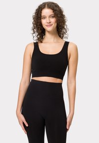 Čern ý crop top s kulatým výstřihem a širokými ramínky, vyrobený z hladké tkaniny. V kombinaci s černými legíny s vysokým pasem.