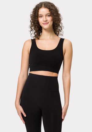 Top corto negro con escote redondeado y tirantes anchos, hecho de una tela suave. Combinado con leggings negros de cintura alta.