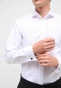 Witte overhemden met een gestructureerde kraag en manchetknopen, aansluitend ontwerp en een gladde textuur; gecombineerd met zwarte broek.