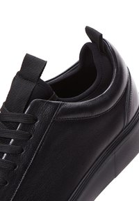 Sneaker in pelle nera caratterizzato da una superficie liscia, punta rotonda, lacci piatti e una suola in gomma con un accento a motivo discreto sul lato.