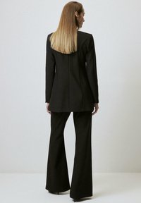 Black tailored blazer with a long silhouette, paired with wide-leg trousers. Smooth texture with structured shoulders and clean lines.