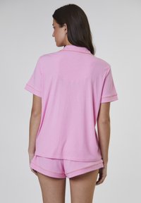 Rosa, kortärmad polo med krage. Tillverkad av mjukt, strukturerat tyg. Matchas med rosa shorts som har upprullade fållar och kontrasterande sömmar.