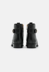 Bottines en cuir noir à texture lisse, avec une fermeture éclair latérale, des accents de quincaillerie dorée et un petit talon bloc.