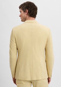 Lichtgele blazer met een subtiele patronenstructuur, enkele split aan de achterkant en een sluiting met twee knopen. Getailleerde fit met lange mouwen.