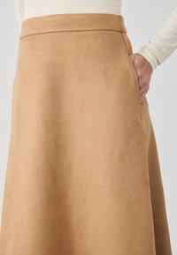 Jupe en suède beige avec une texture lisse, silhouette en A, taille haute et poches latérales. Présente des lignes épurées et un design minimaliste.