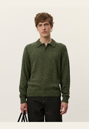 Green knitted sweater with a polo collar, textured fabric, ribbed hem, and one-button closure, paired with dark jeans and a black bag.