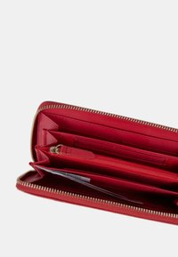 Portafoglio in pelle rossa con chiusura a zip, dotato di più slot per carte, scomparti e una piccola tasca con zip. Texture liscia.