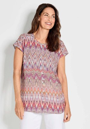 Korte mouwen blouse met een multicolor zigzagpatroon in roze, paars en wit; ronde halslijn; vijf knopen aan de voorkant.