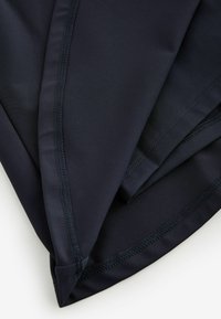 Gros plan sur un tissu noir avec des coutures renforcées disposées en diagonale sur un fond clair.