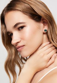 Pendientes de botón cuadrados con esmeralda de color verde oscuro, engastados en metal de tono plateado, con un acabado pulido y un diseño geométrico.