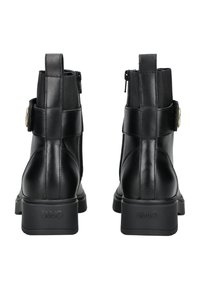 Botas de tobillo de cuero negro con una textura suave, que presentan un zipper lateral, herrajes en tono dorado y una suela de goma gruesa.