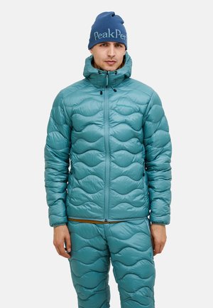 Teal puffer jacket with a quilted wave pattern, hood, and zip closure. Paired with matching quilted pants. Blue knit beanie with logo.