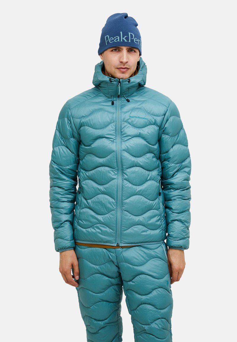 Teal pufferjack met een gequilte golfpatroon, capuchon en ritssluiting. Gecombineerd met bijpassende gequiltte broek. Blauw gebreid mutsje met logo.