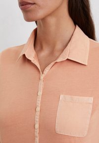 Perzikkleurig button-up shirt met een kraag, voorzien van een enkele borstzak en een zachte, gestructureerde stof.