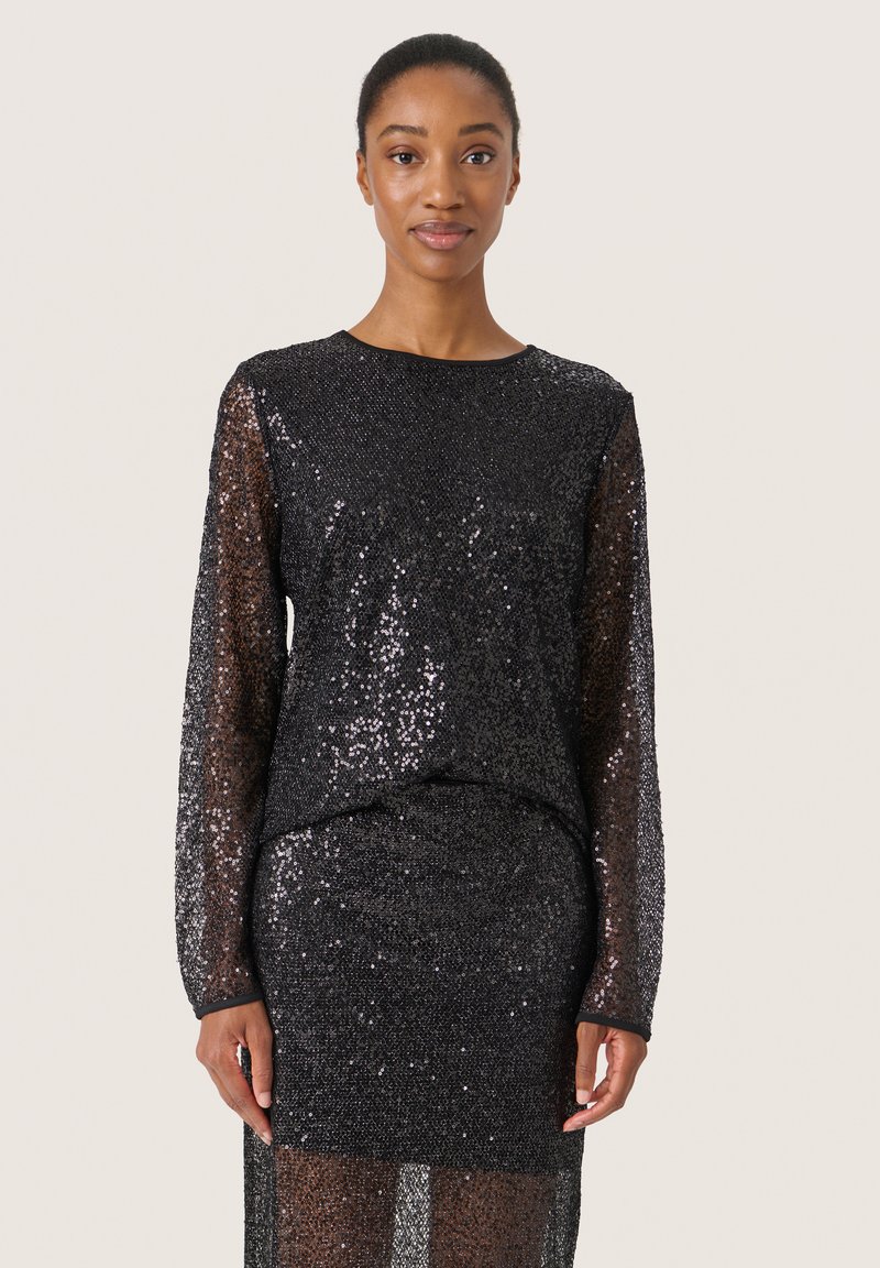 Abito nero a paillettes con maniche lunghe, scollo rotondo e silhouette aderente. Texture scintillante, design a strati che accentua il movimento.