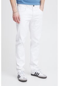 Jeans de mezclilla blanca de corte recto, con bolsillos cosidos y cierre de botón único; combinados con zapatillas en tonos gris y negro.
