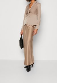 Beige satinblus med vriden front och långa ärmar, tillsammans med en beige satinkjol, svarta spetsiga klackar och en svart handväska.