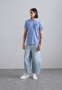 Light blue cotton t-shirt with a round neckline and a small graphic on the chest, paired with loose-fitting light blue denim jeans and white sneakers.