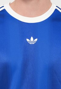 Μπλε αθλητική μπλούζα με λευκή λαιμόκοψη. Κάθετες ρίγες και λευκό λογότυπο Adidas στην αριστερή πλευρά. Λείο, συνθετικό ύφασμα.